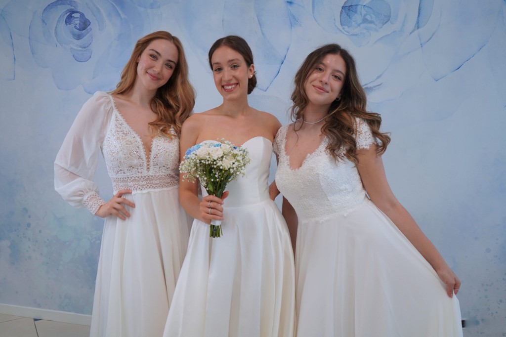 Tre spose in abito bianco nell'atelier, sfondo floreale azzurro